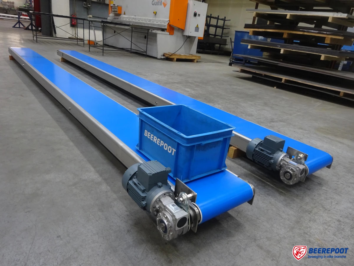 Je ziet twee blauwe transportbanden van Beerepoot. Op de voorste transportband staat een blauw Beerepoot kratje. De transportbanden liggen in een voorraadhal van Beerepoot.