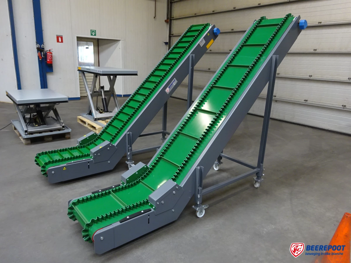 Je ziet twee groene opvoer transportbanden van Beerepoot in een voorraadhal van Beerepoot. Op de achtergrond staan twee kleine heftafels van Beerepoot.