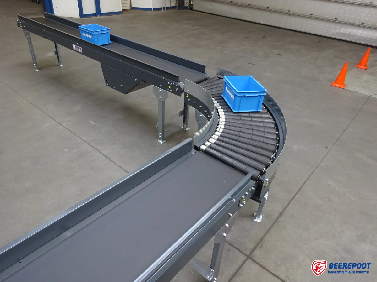Je ziet een deel van een nieuwe grijze transportband uitgestald in een voorraadhal van Beerepoot. Op de transportband staan twee blauwe kratjes van Beerepoot.