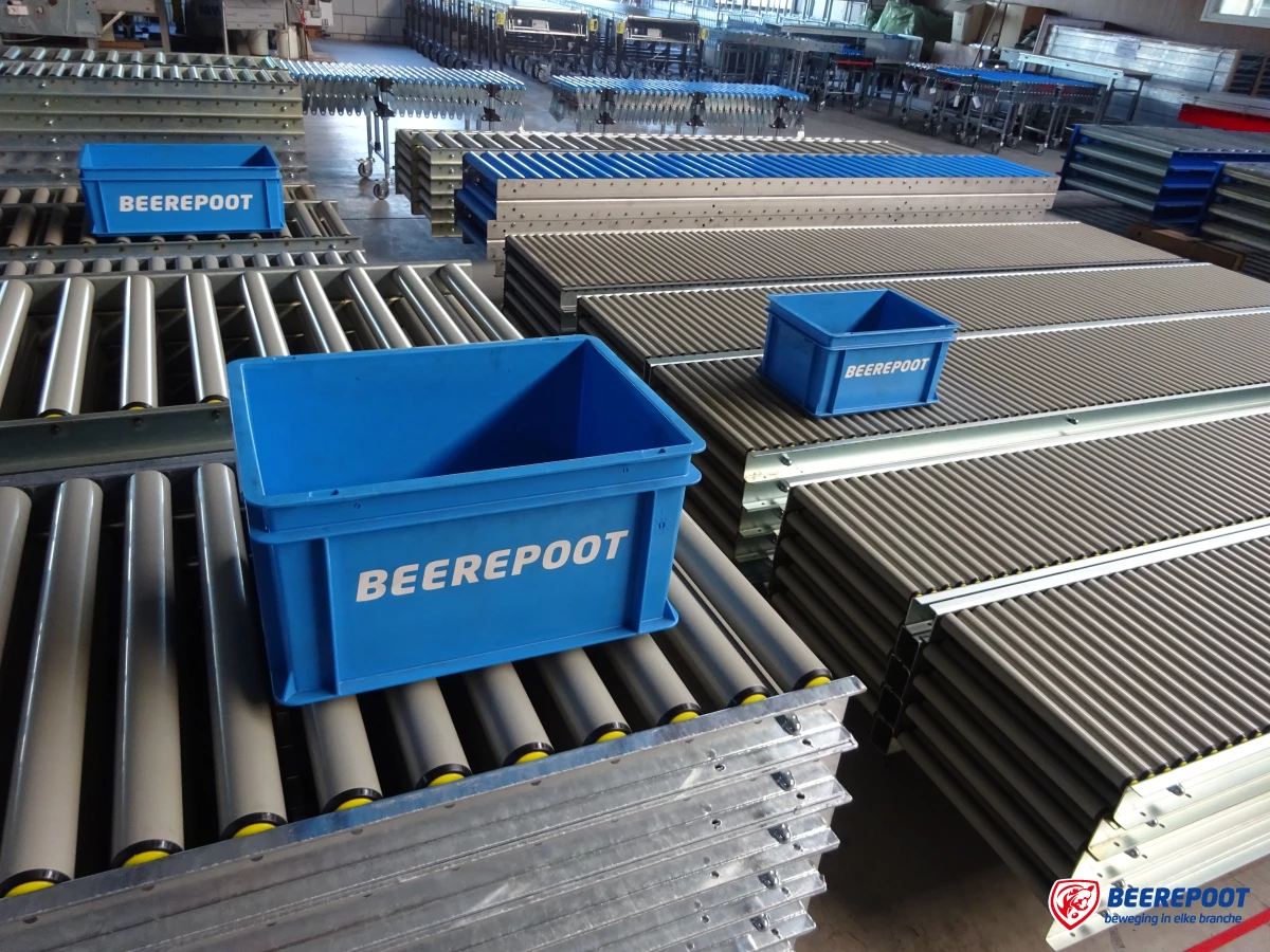 We zien veel stapels gebruikte grijze rollenbanen naast en achter elkaar met daarop blauwe Beerepoot kratjes. De rollenbanen staan in een voorraadhal van Beerepoot.