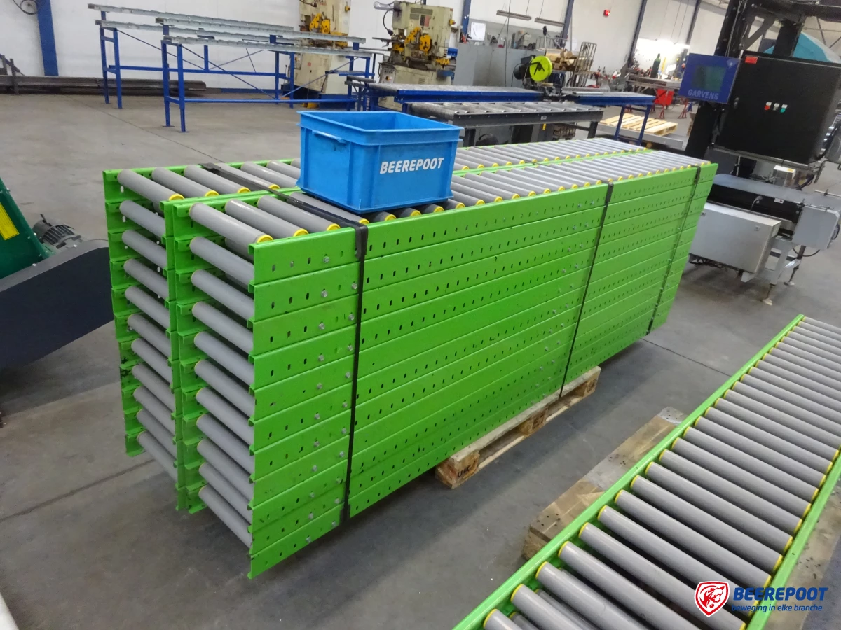 We zien een stapel groene rollenbanen met daarvoor een enkele groene rollenbaan. Op de stapel rollenbanen een blauw Beerepoot kratje. De rollenbanen staan in de werkplaats van Beerepoot.