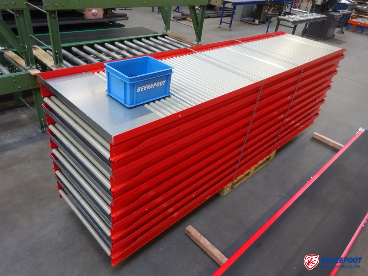 Je ziet een stapel niet aangedreven rode rollenbanen met daarop een blauw Beerepoot kratje. Erachter staat een groene rollenbaan. De stapel rollenbanen staat in een voorraadhal van Beerepoot