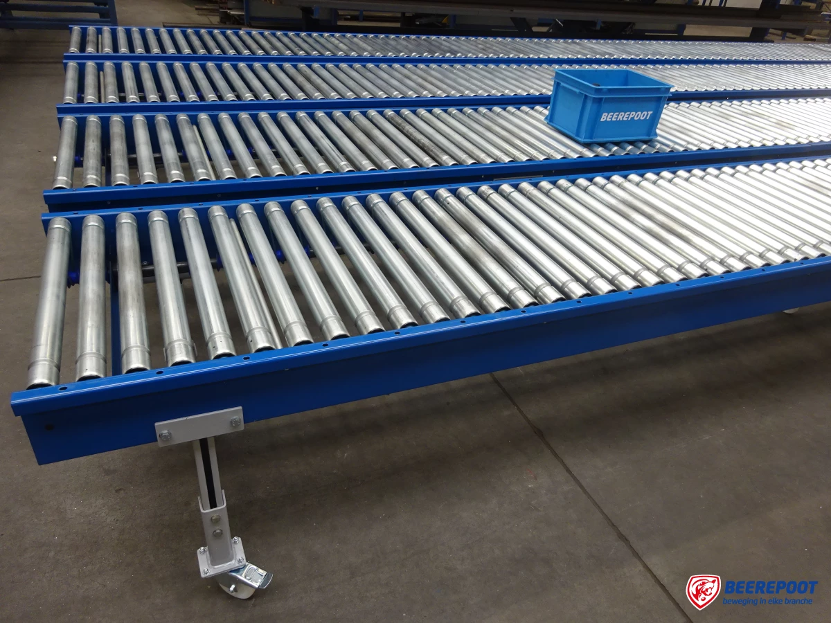 Je ziet drie blauwe niet aangedreven rollenbanen op een rijtje met op de middelste rollenbaan het blauwe Beerepoot kratje